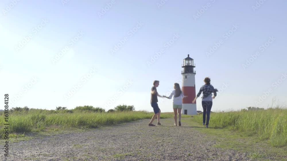 Excited Multiethnic Group Of Teens Run, Twirl, Toward Picturesque Lighthouse Excited Multiethnic Group Of Teens Run, Twirl, Toward Picturesque Lighthouse