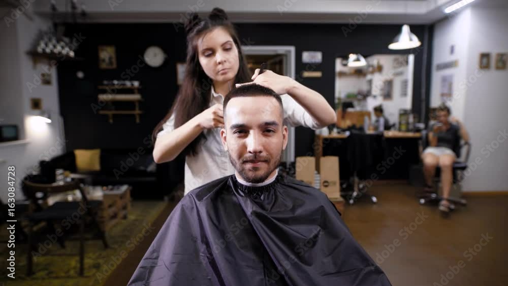 Woman making haircut to stylish handsome client sitting in barber salon Woman making haircut to stylish handsome client sitting in barber salon