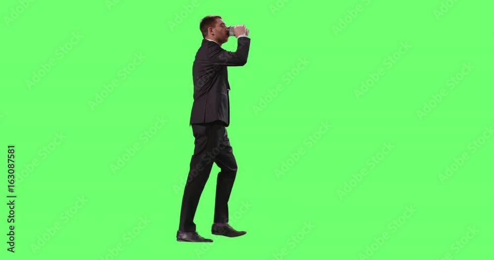 Tired Businessman in a Suit is Walking with a Coffee on a Mock-up Green Screen in the Background. Tired Businessman in a Suit is Walking with a Coffee on a Mock-up Green Screen in the Background.