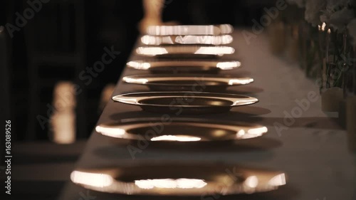 Waiter hand sillhuette puts forks near empty dinner plates on banquette table in semi dark dining room photo