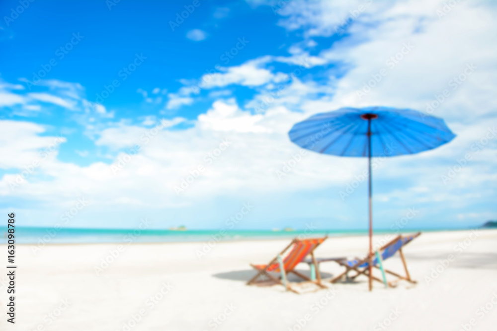 Blurred image of beach chairs and parasol on white sand beach in summer blue sky background
