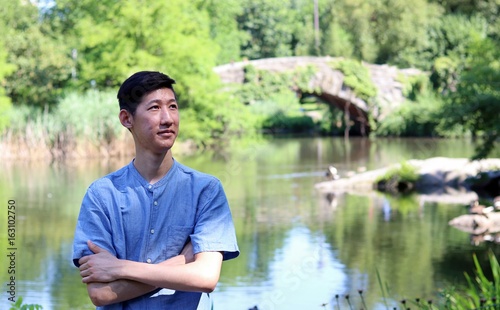 Young handsome asian man smiling looking right, standing by scenic wildlife nature pond waterfront