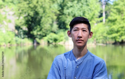 Close up of young handsome asian man looking up standing by scenic wildlife nature pond waterfront