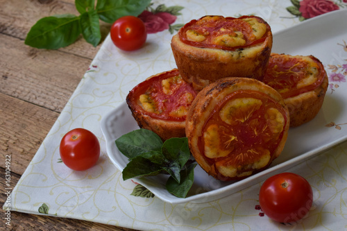 Salty snack. Homemade muffins with cheese, tomatoes and basil on wooden background. Savory pastry.