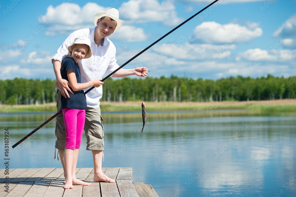 Dad helps daughter to catch fish with a fishing rod on the river Dad helps daughter to catch fish with a fishing rod on the river