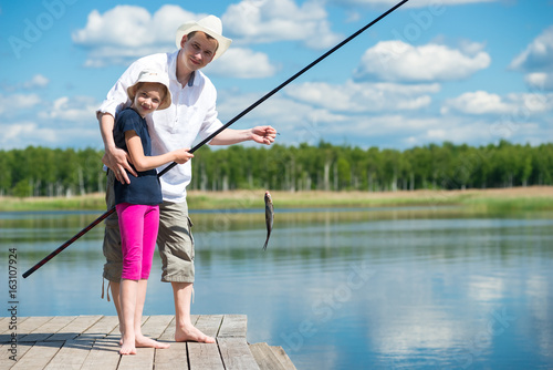 Dad helps daughter to catch fish with a fishing rod on the river