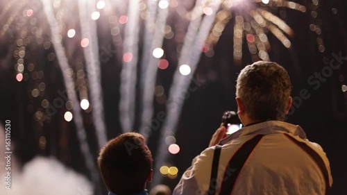 Unrecognizable father and son filming and watching fireworks