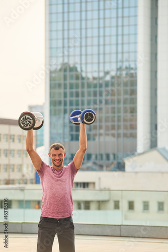 Man holding hoverboards and smiling. Happy guy, urban background.