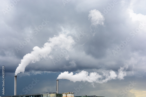 Industrial smoke emission from factory chimney under a stormy sky. © olrat