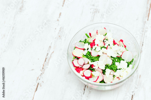 Fresh vegetable salad in a glass bowl on white wooden background with copy space