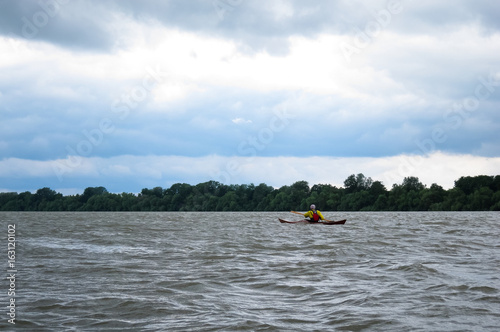 Man in selfmade wooden kayak in Danube river against background of storm sky. Kayaking in nature reserve of Danube Delta
