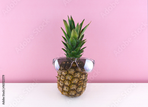 Ripe pineapple wearing sunglasses on pink background.