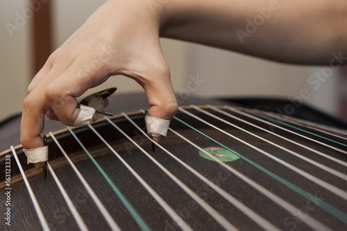 A girl is playing Guzheng.The guzheng or gu zheng, also simply called zheng, is a Chinese plucked zither. It has 18 or more strings and movable bridges.