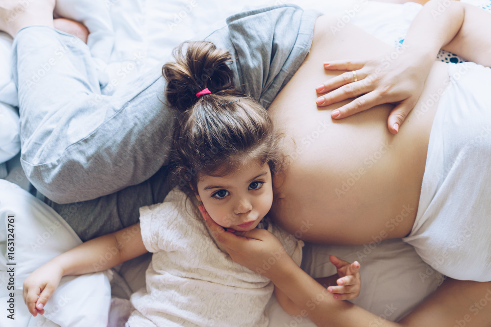 Beautiful pregnant woman and her cute little daughter together in bed