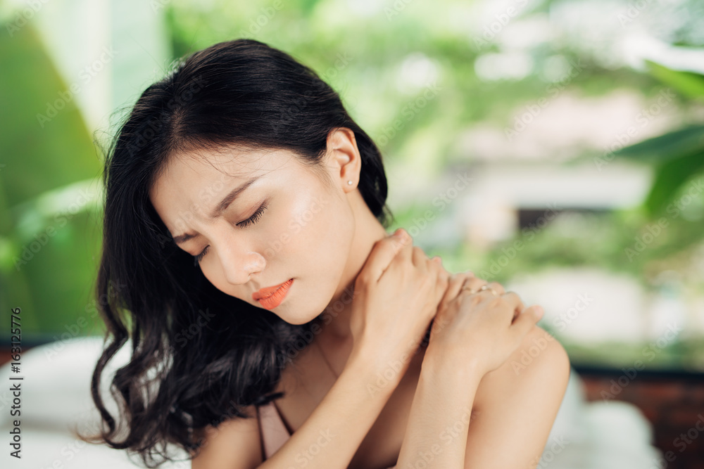Young asian woman suffering from neck pain while sitting on bed at home Young asian woman suffering from neck pain while sitting on bed at home