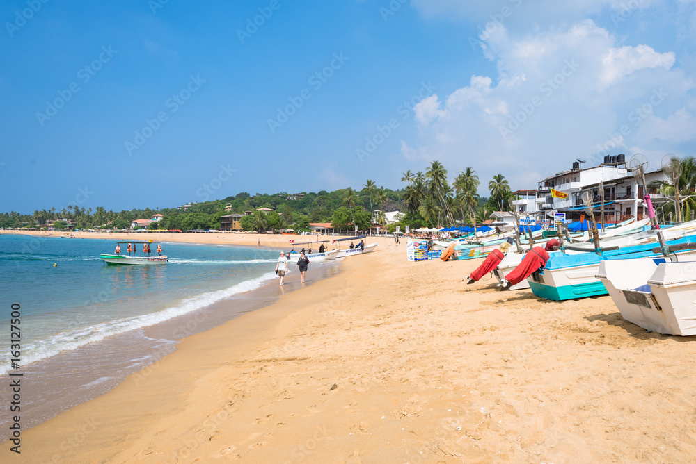 At the beach of one of the major tourist spots in the south west of Sri Lanka. Tourist do sunbathing and aquatic sports. Outrigger and traditional fishing boats on the beach