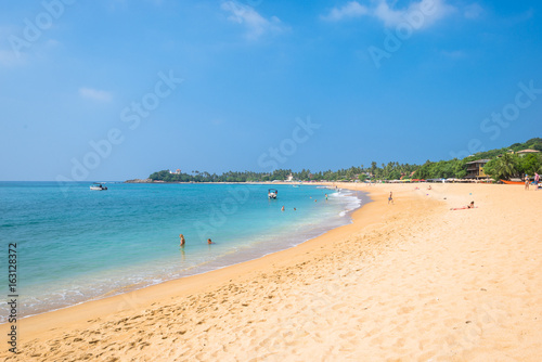 At the beach of one of the major tourist spots in the south west of Sri Lanka. Tourist do sunbathing and aquatic sports. Outrigger and traditional fishing boats on the beach
