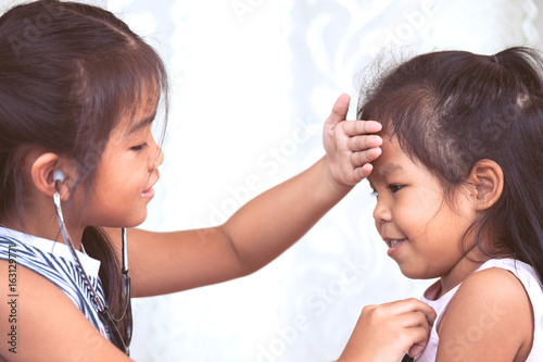 Two cute asian little child girls playing doctor and patient together in vintage color tone
