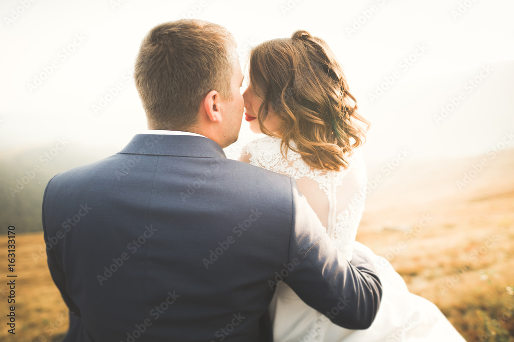 Young newly wed couple, bride and groom kissing, hugging on perfect view of mountains, blue sky Young newly wed couple, bride and groom kissing, hugging on perfect view of mountains, blue sky