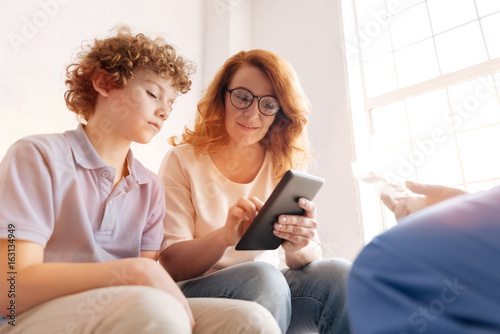 Positive delighted mother showing tablet to her son