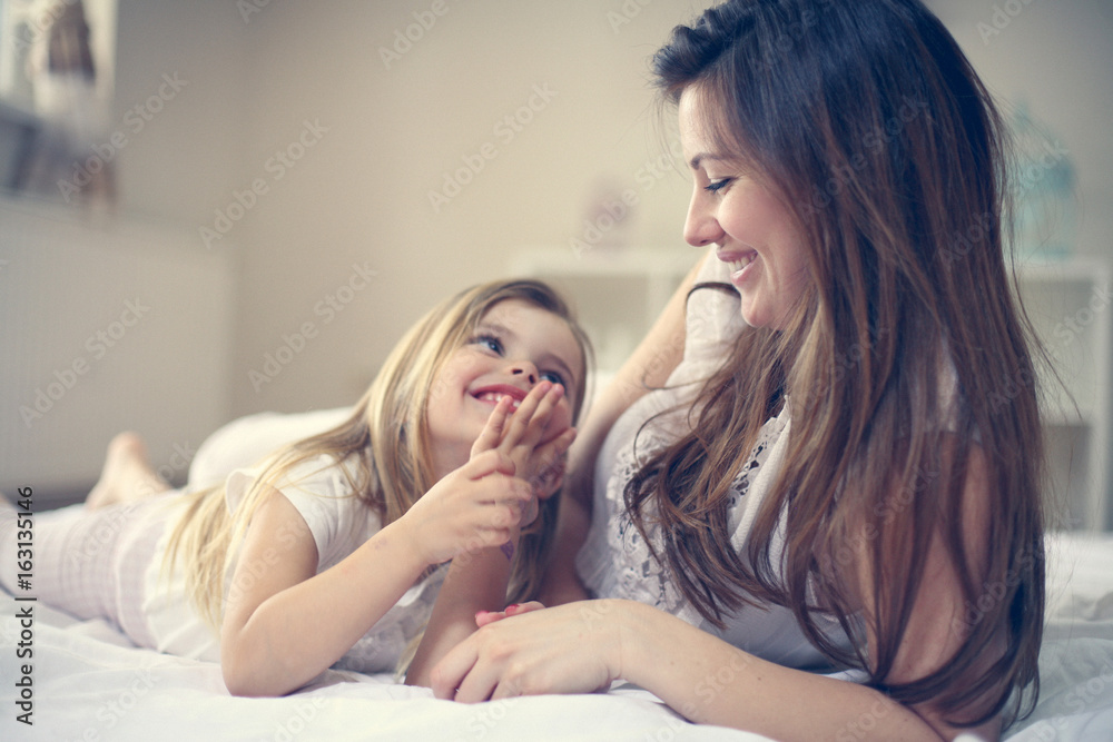 Mother with her cute little daughter on bed.