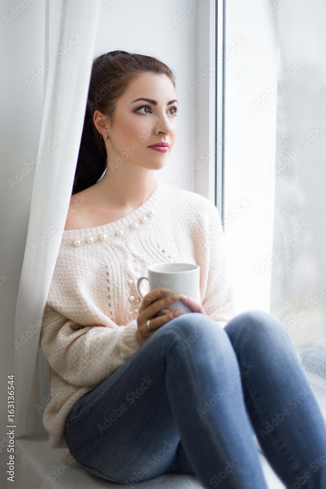 cute young woman drinking coffee and looking out of the window cute young woman drinking coffee and looking out of the window