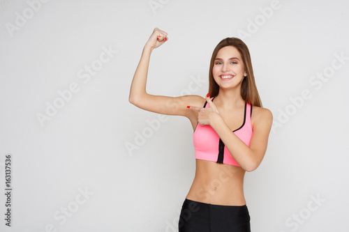 Smiling fitness woman shows her muscular hand