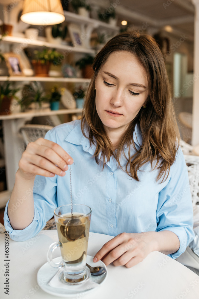 A young woman sits in a cozy light kitchen at the table and makes herself a tea A young woman sits in a cozy light kitchen at the table and makes herself a tea
