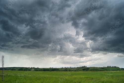 Storm cyclone over summer fields, hills and forests