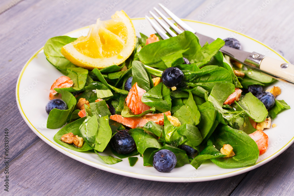 Salmon, spinach, blueberries and walnuts salad on white plate Salmon, spinach, blueberries and walnuts salad on white plate