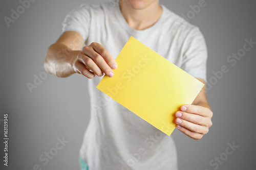 A man in a gray t-shirt holding blank clear yellow of the sheet. Closeup. Isolated
