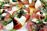 Caprese salad. Sliced tomatoes, mozzarella and shredded basil, poured with oil and vinegar, sprinkled with salt and colour pepper laying on white plate.