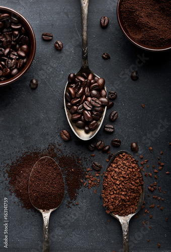 Three kinds of coffee in spoons and cups over dark background. 