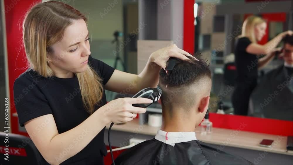 Female hairdresser at work. She trimming the hair by hair clipper. Male customer sitting on the chair Female hairdresser at work. She trimming the hair by hair clipper. Male customer sitting on the chair