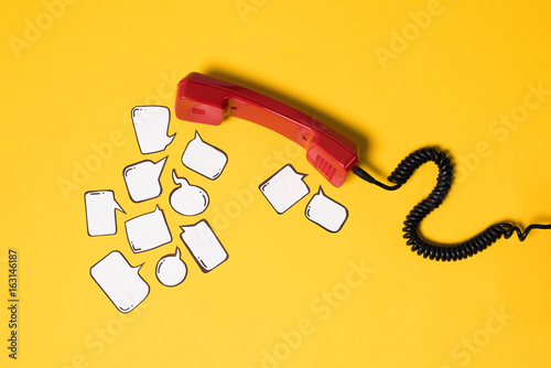 Close-up view of red telephone handset and blank speech bubbles isolated on yellow