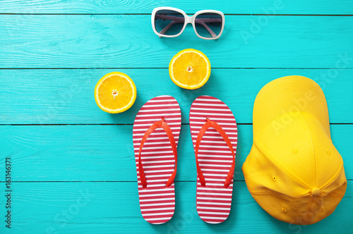 red striped flip flops, red sunglasses and orange fruit on blue wooden background. Top view and summer time.