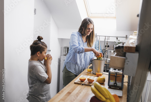 Mother making orange juice for her son at kitchen.
