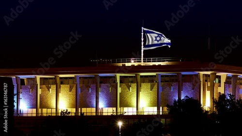 Knesset building the Parliament of Israel with flying waving flag of Israel at night. The Knesset located in Jerusalem and elects both President and Prime Minister and supervises Israeli government photo