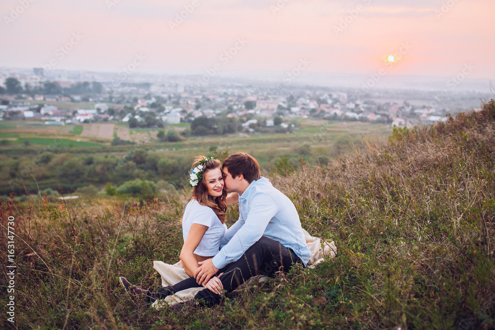 couple, love, nature and people concept - happy loving couple sitting on a plaid in a field on a background of magical sunset couple, love, nature and people concept - happy loving couple sitting on a plaid in a field on a background of magical sunset