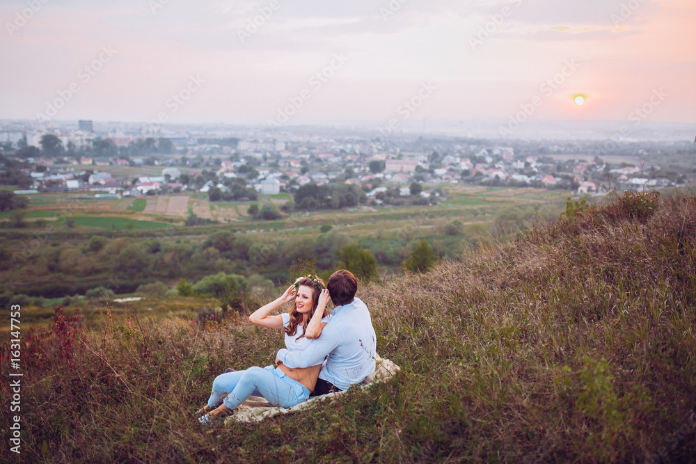 couple, love, nature and people concept - happy loving couple sitting on a plaid in a field on a background of magical sunset couple, love, nature and people concept - happy loving couple sitting on a plaid in a field on a background of magical sunset