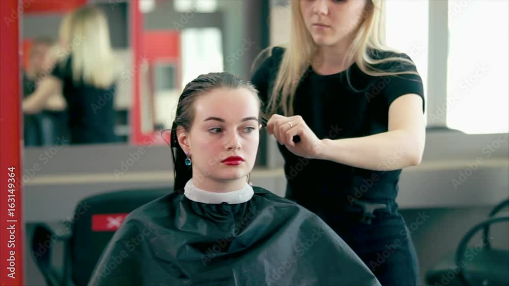 A young and experienced hair stylist who goes through the practice in a beauty salon combs his wet hair in order to dry his hair with a hairdryer and make stylish curls. A young and experienced hair stylist who goes through the practice in a beauty salon combs his wet hair in order to dry his hair with a hairdryer and make stylish curls.