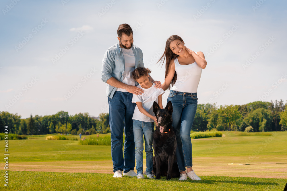 Obraz premium Happy multiethnic family standing with dog on green lawn