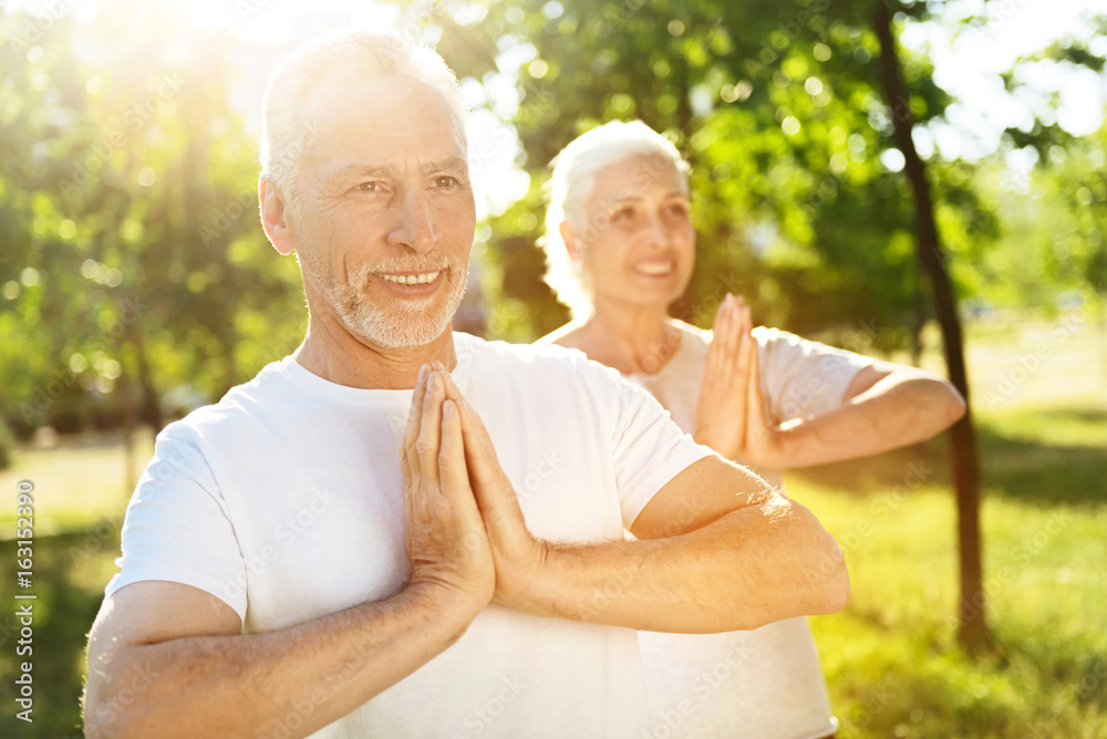 Delighted aged couple meditating in the park Delighted aged couple meditating in the park