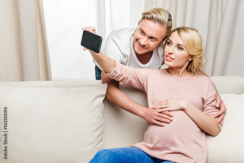 Happy pregnant woman with husband taking selfie with smartphone at home Happy pregnant woman with husband taking selfie with smartphone at home