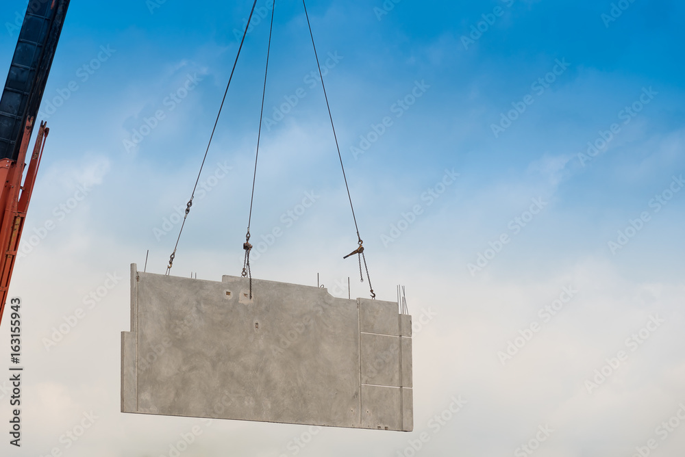 Construction site crane is lifting a precast concrete wall panel. Stock