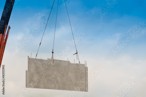 Construction site crane is lifting a precast concrete wall panel.