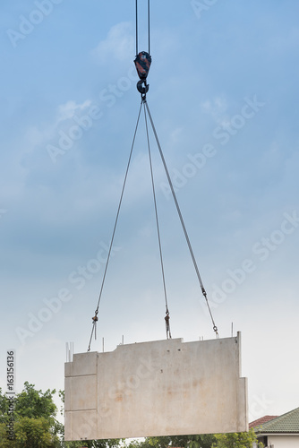 Construction site crane is lifting a precast concrete wall panel.