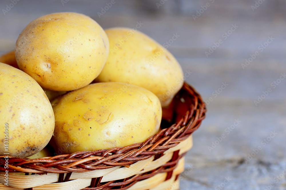 Raw potatoes harvest. Fresh raw potatoes in a wicker basket on a vintage wooden background. Closeup Raw potatoes harvest. Fresh raw potatoes in a wicker basket on a vintage wooden background. Closeup