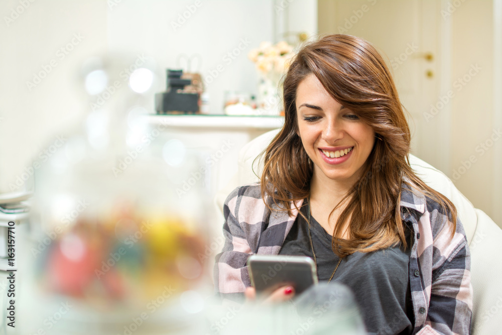 Portrait of smiling young woman using mobile phone while sitting on sofa at home. Portrait of smiling young woman using mobile phone while sitting on sofa at home.