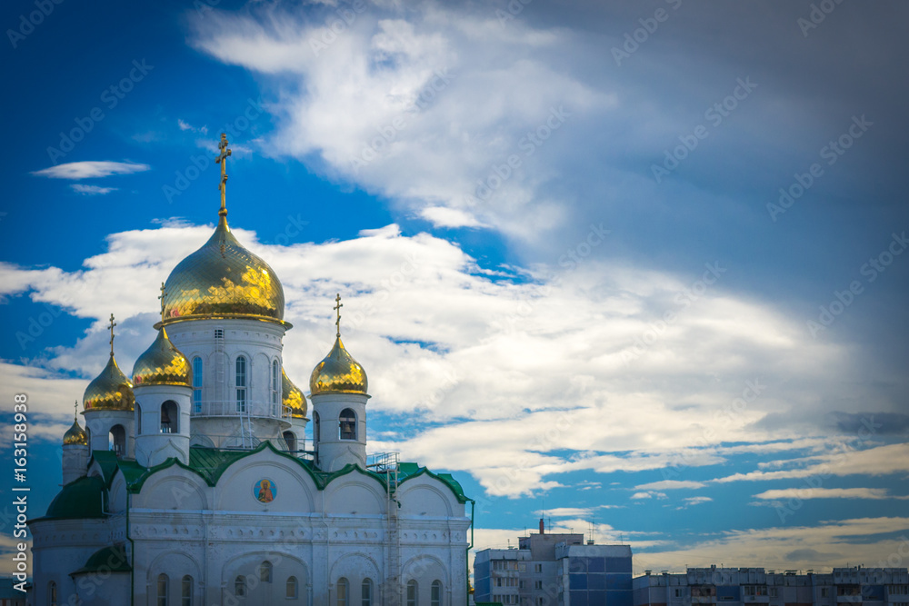 Shining golden domes of a Russian Orthodox Church in Barnaul with dramatic clouds on blue sky in summer afternoon